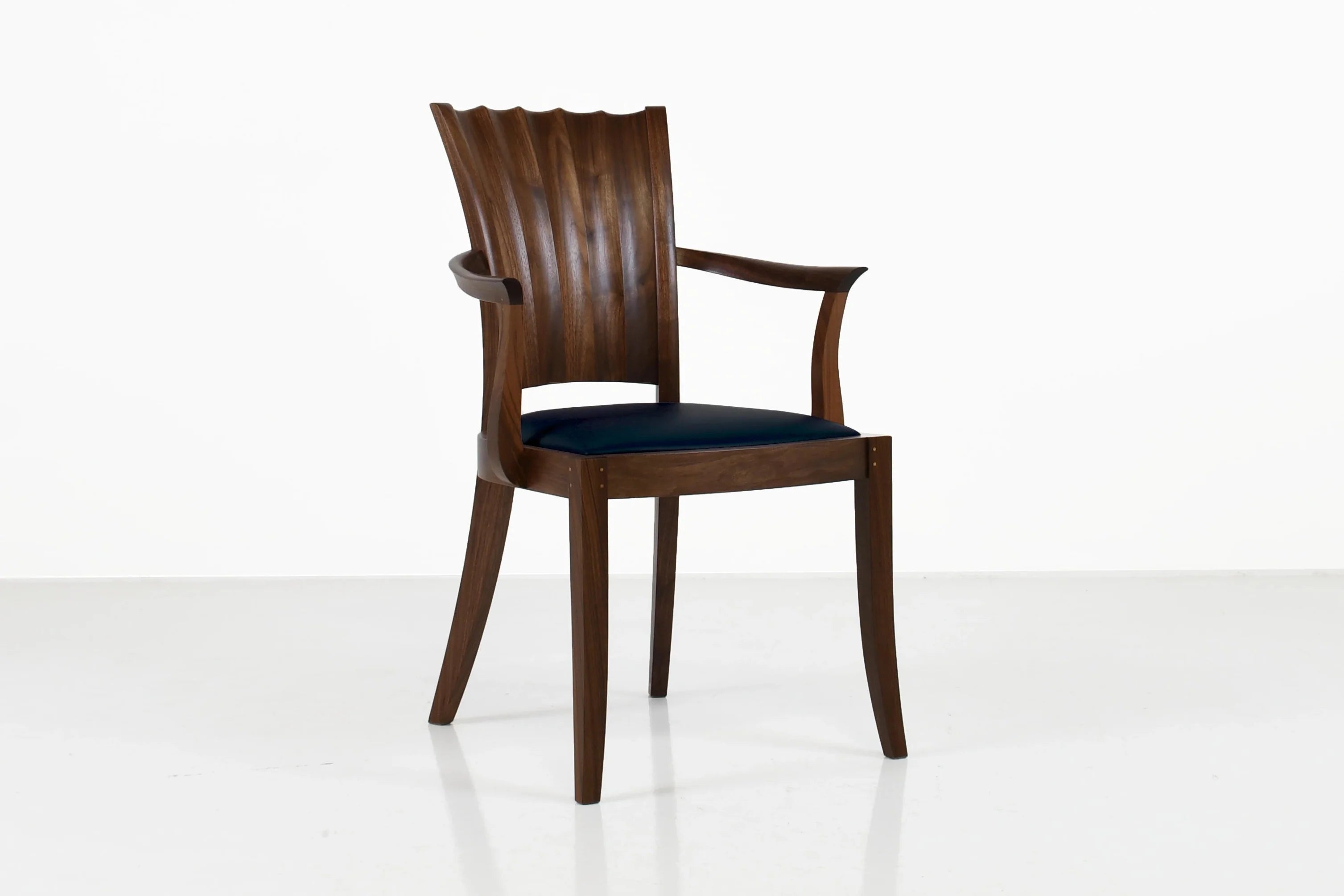 Fauteuil - Les lignes sablier de son dossier unique se dessinent dans les courbes convexes et concaves sculptées à la main.