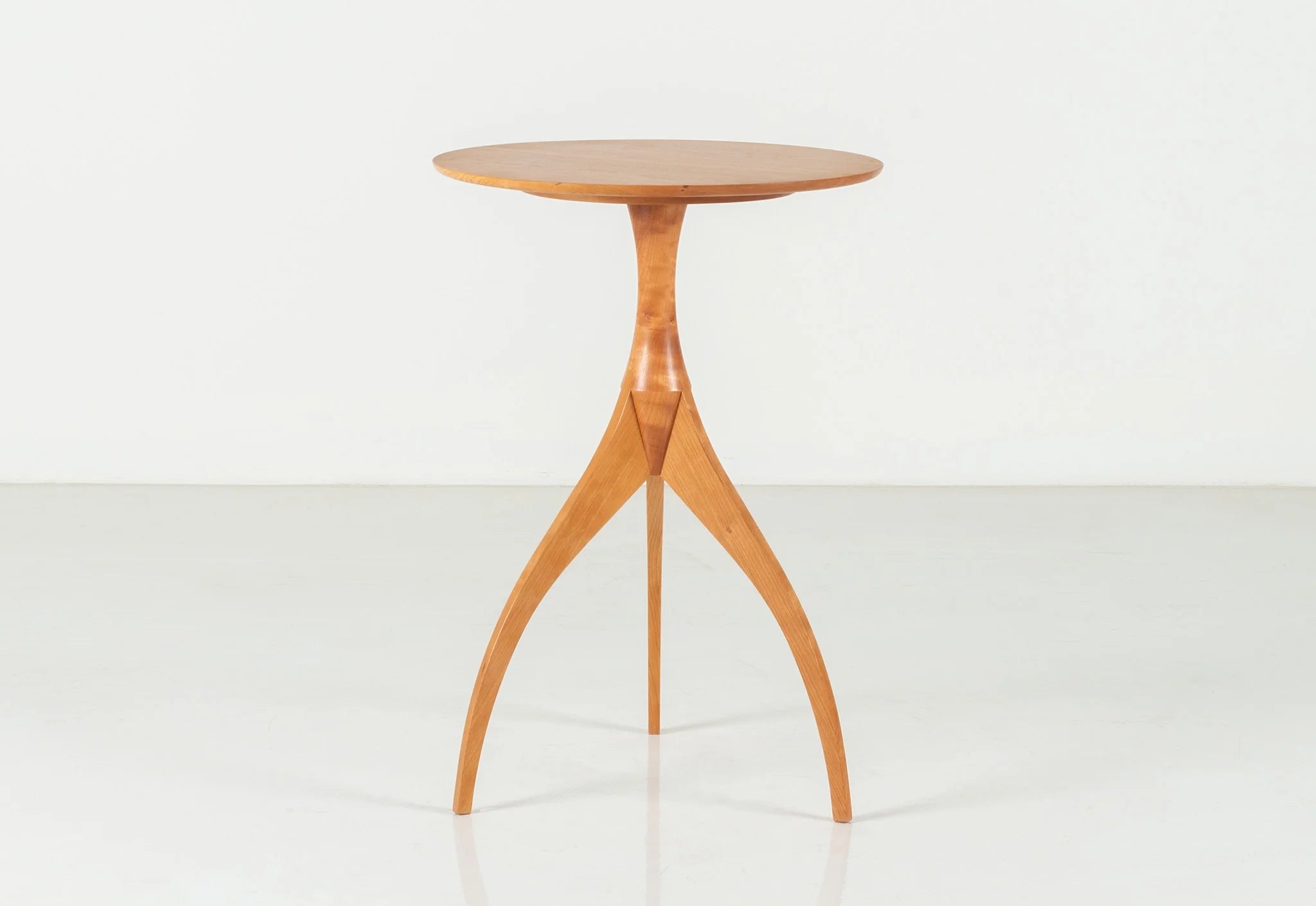 Table - Fabriquée en bois massif, finie à la main, la table est dotée de trois pieds qui s'arquent en s'élevant, formant une inverse