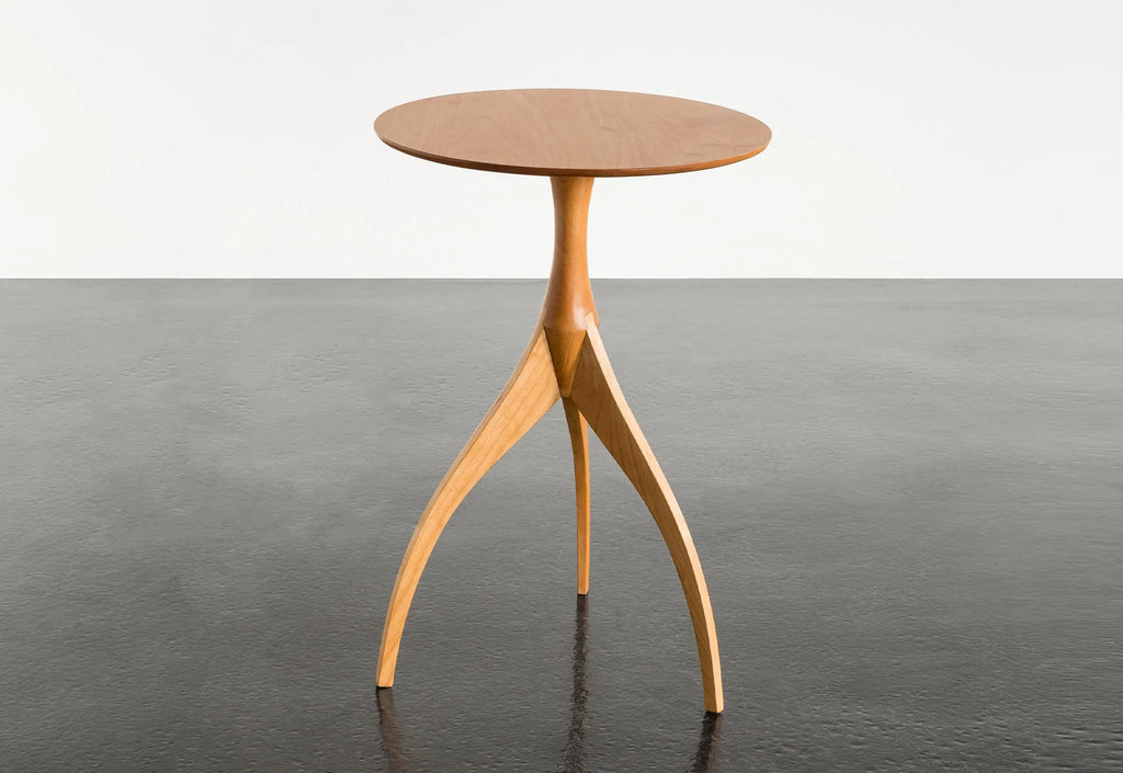 Table - Fabriquée en bois massif, finie à la main, la table est dotée de trois pieds qui s'arquent en s'élevant, formant une inverse