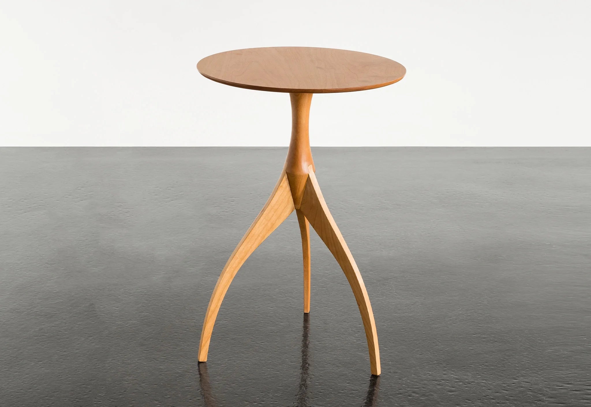 Table - Fabriquée en bois massif, finie à la main, la table est dotée de trois pieds qui s'arquent en s'élevant, formant une inverse