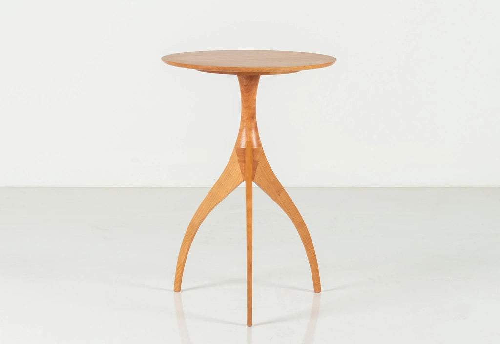 Table - Fabriquée en bois massif, finie à la main, la table est dotée de trois pieds qui s'arquent en s'élevant, formant une inverse