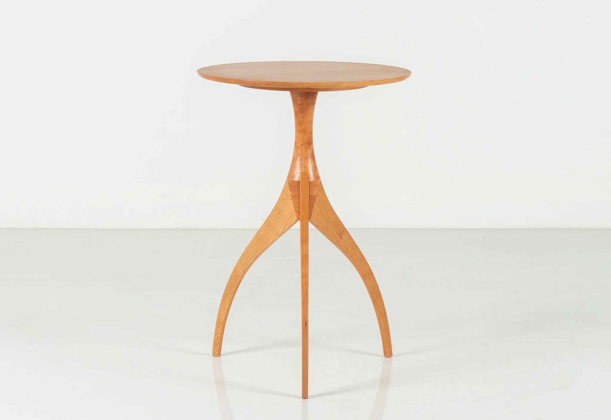 Table - Fabriquée en bois massif, finie à la main, la table est dotée de trois pieds qui s'arquent en s'élevant, formant une inverse