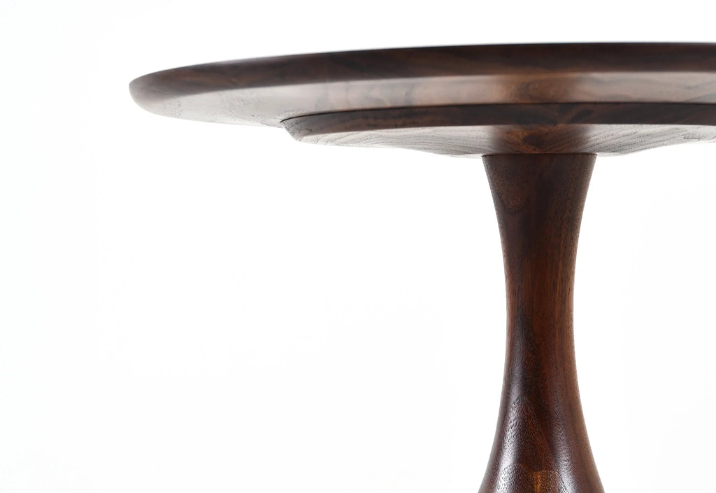 Table - Fabriquée en bois massif, finie à la main, la table est dotée de trois pieds qui s'arquent en s'élevant, formant une inverse