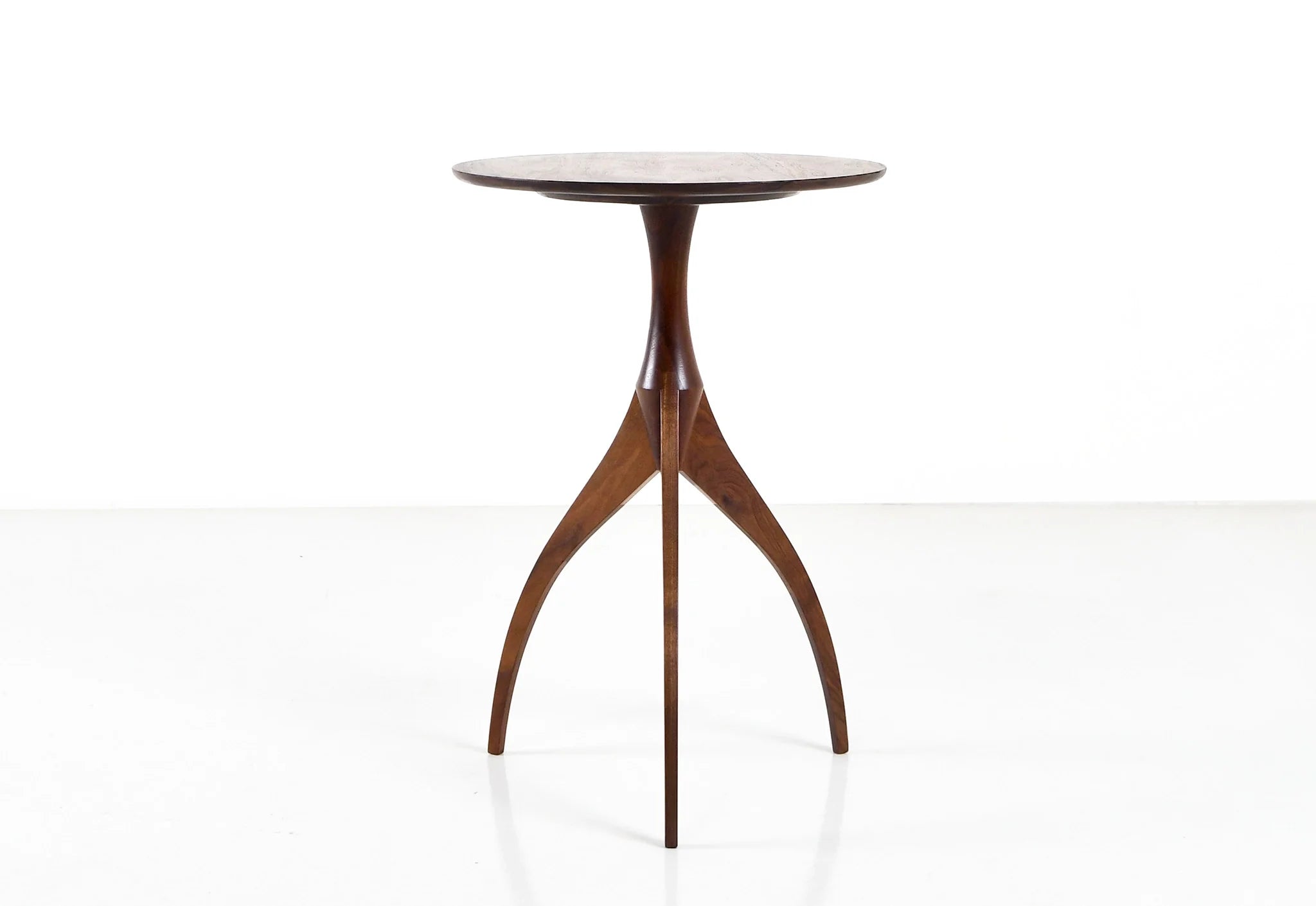 Table - Fabriquée en bois massif, finie à la main, la table est dotée de trois pieds qui s'arquent en s'élevant, formant une inverse