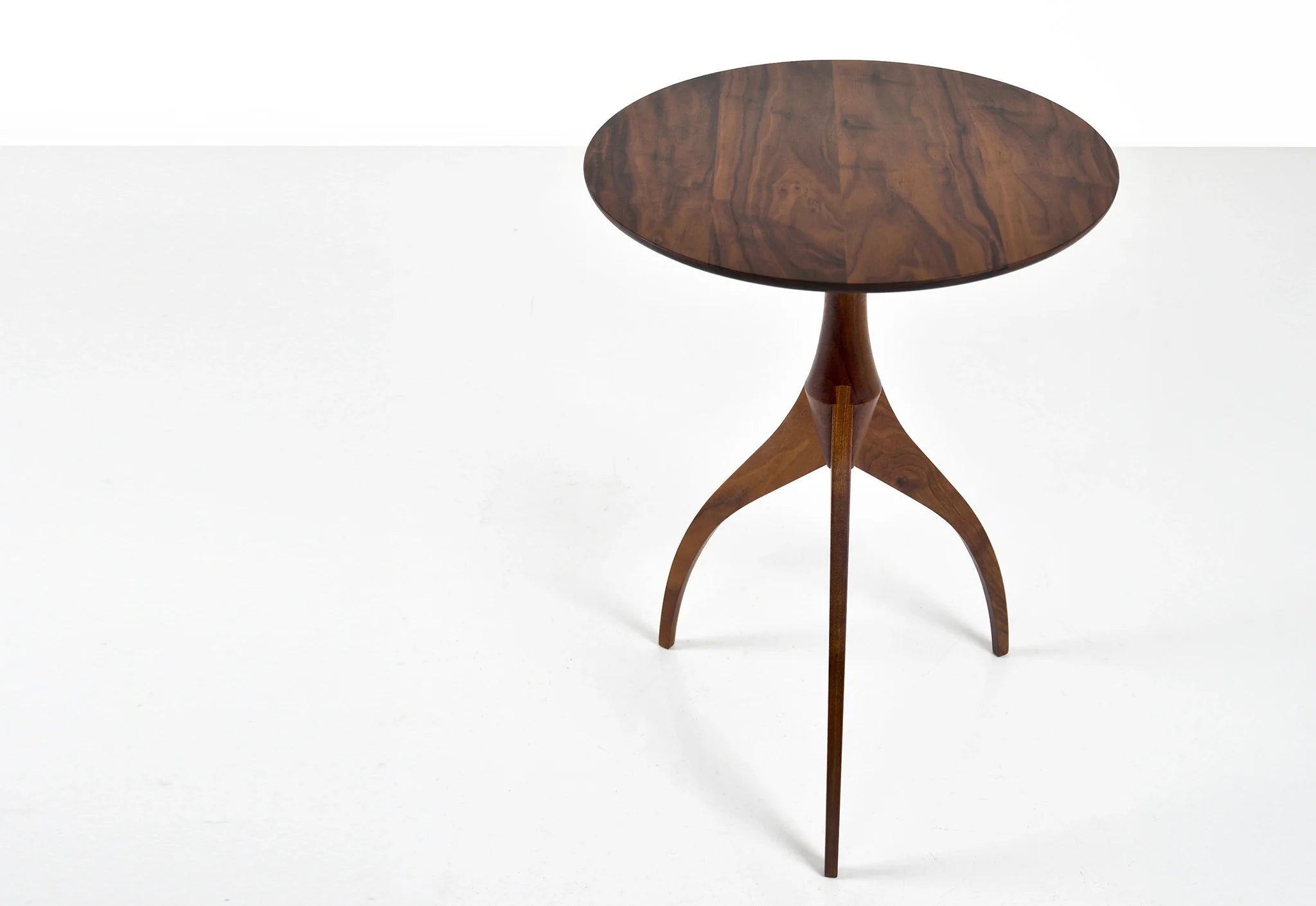 Table - Fabriquée en bois massif, finie à la main, la table est dotée de trois pieds qui s'arquent en s'élevant, formant une inverse